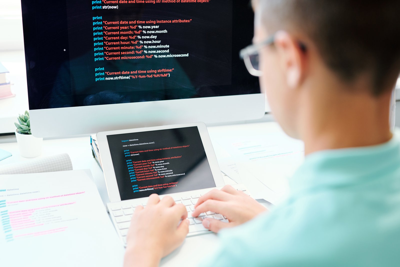 Developer writing code on a tablet and monitor at a desk